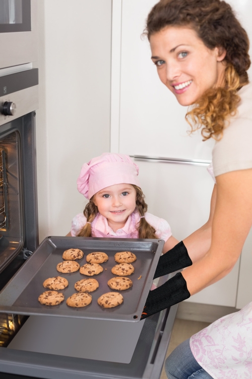 woman removing cookies from oven while girl looks on